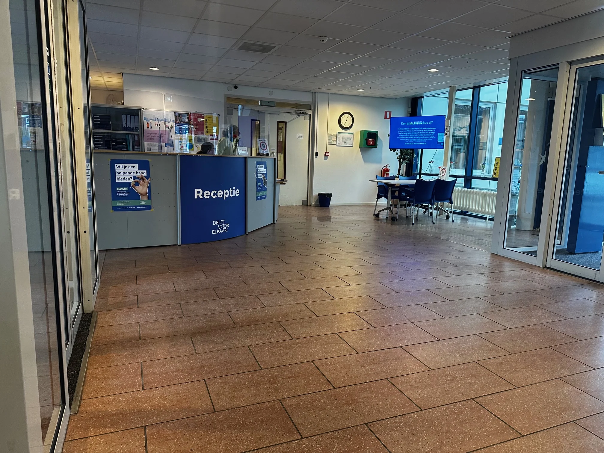 Receptiebalie in de entreehal van een gebouw aan de Van Bleyswijckstraat met informatieposters en wachtruimte.